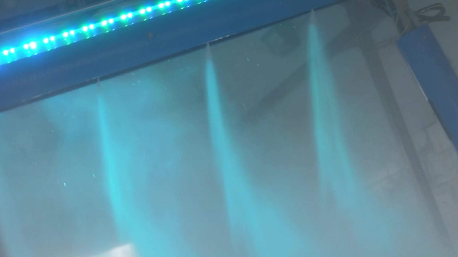 High-pressure rinse jets spraying a curtain of water under blue and green LED lighting in a touchless wash bay