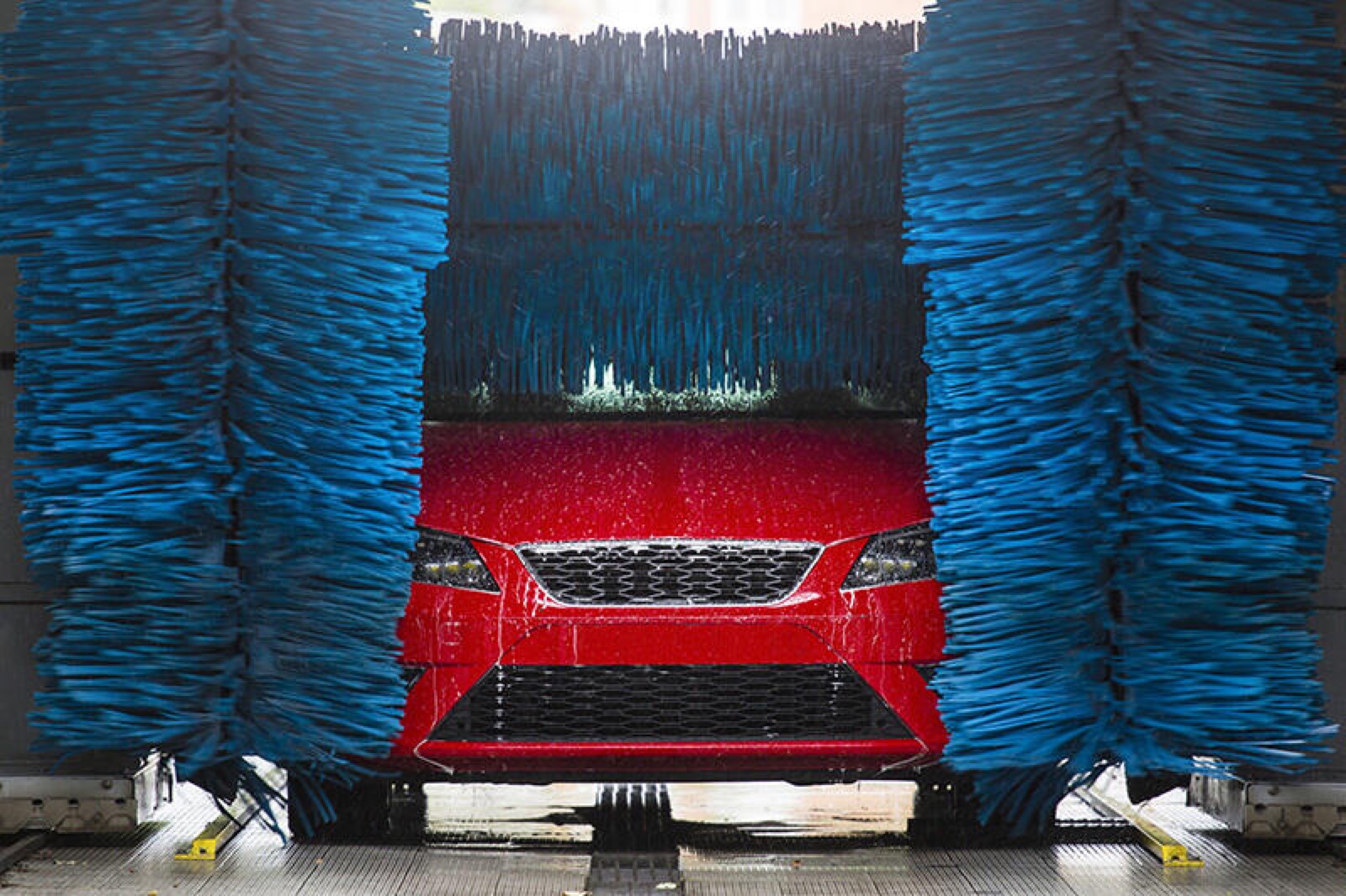 Red car being scrubbed by spinning blue brushes in a friction car wash