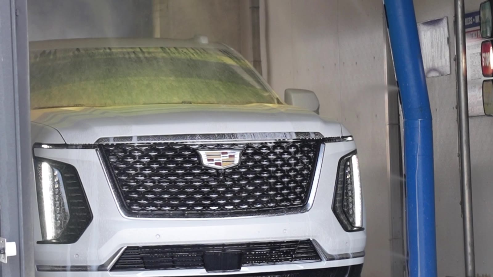 White SUV with presoak detergent clinging to its windshield and hood inside an Al's Super Wash touchless bay